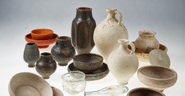 Mehrere Keramikgefäße in verschiedenen Größen und Farben sowie kleinere Glasgefäße stehen auf einem weißen Untergrund.