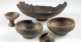 Mehrere dunkelbraune Keramikgefäße in unterschiedlichen Größen liegen nebeneinander auf einem weißen Untergrund.