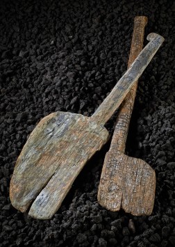 Zwei alte Schaufeln aus Holz liegen auf schwarzen Kieseln